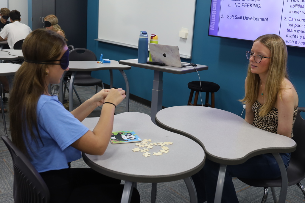 Two students working on a puzzle, one blindfolded 