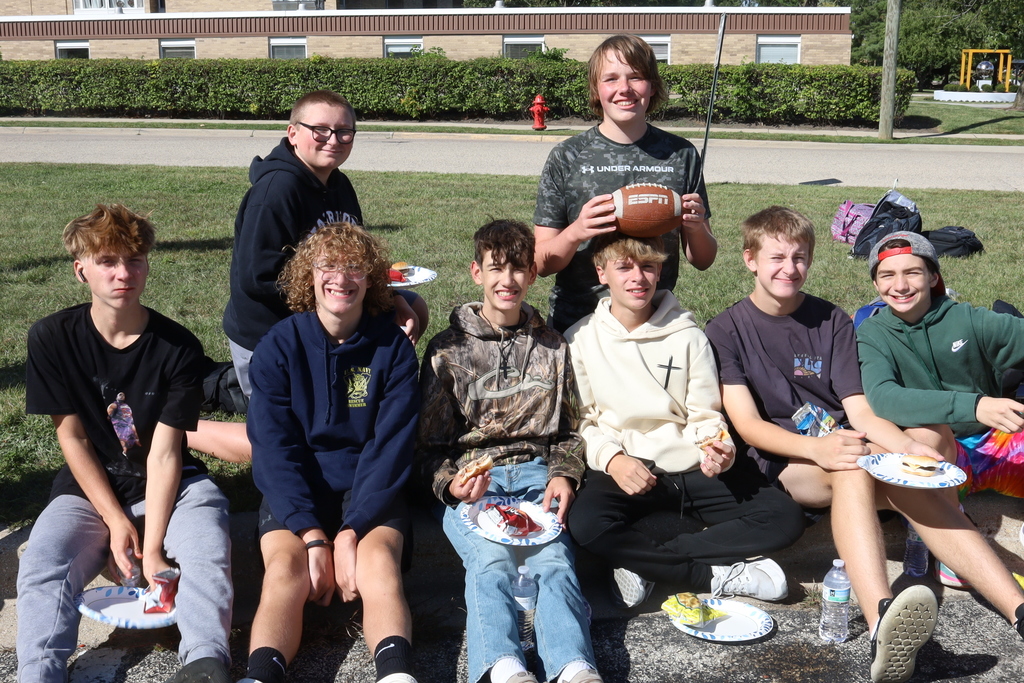 Students on the ground smiling with their food, one holding a football
