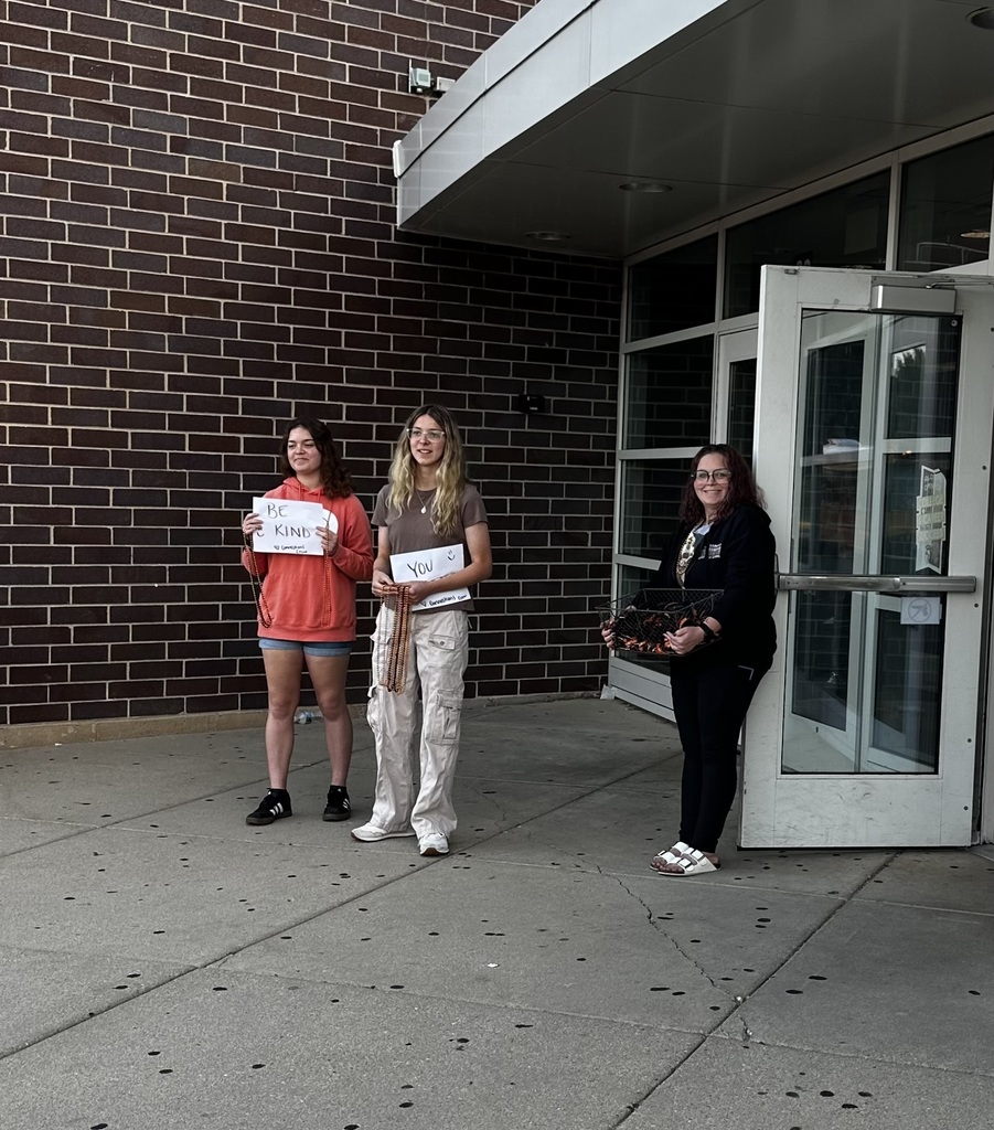 Students at the entrance. holding a sign that says "Be Kind" and beads