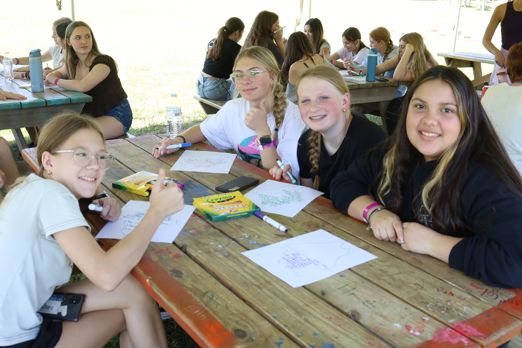 Students drawing with marker and smiling at a picnic table