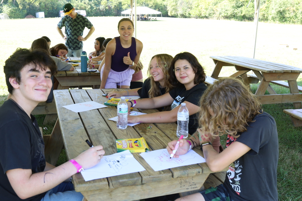 Students smiling at a picnic table drawing with markers