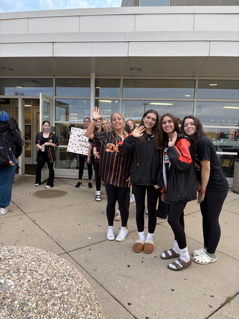A few members from dance team waving in front of the school