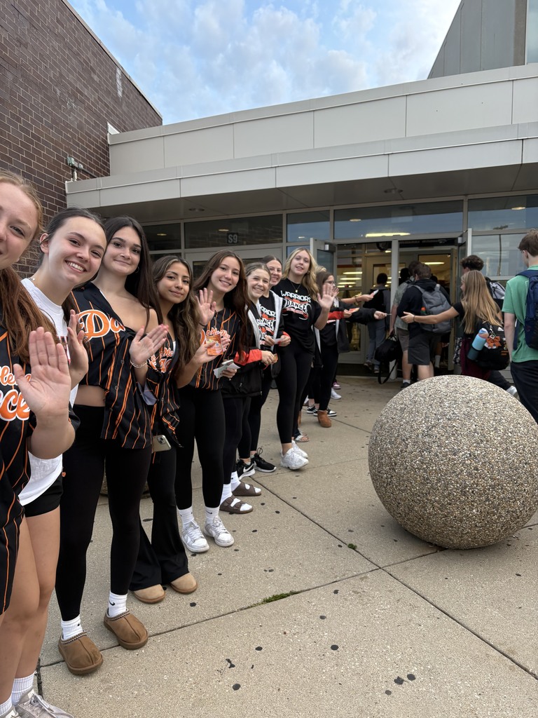 Dance team lined up waving by the front of the school