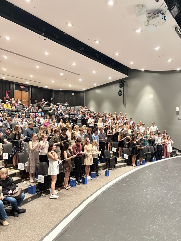 Students in the auditorium standing and holding papers