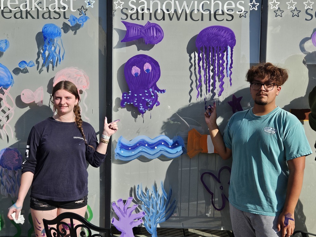 Photos of students painting storefront windows in downtown McHenry to celebrate the start of homecoming with a parade