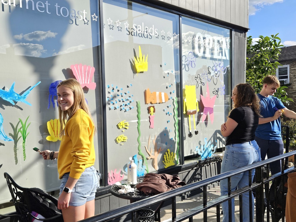Photos of students painting storefront windows in downtown McHenry to celebrate the start of homecoming with a parade
