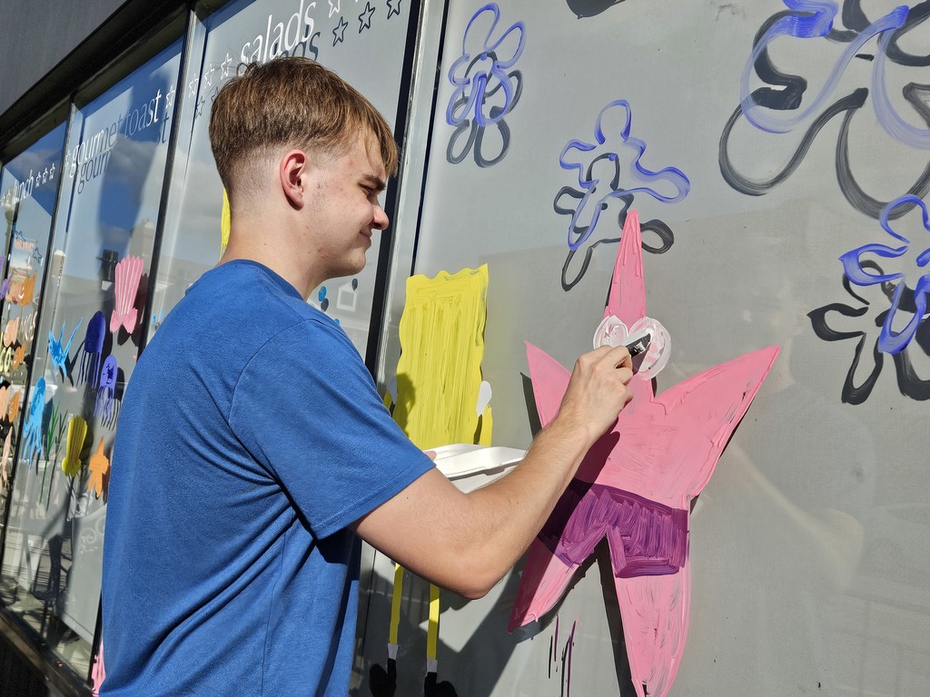 Photos of students painting storefront windows in downtown McHenry to celebrate the start of homecoming with a parade