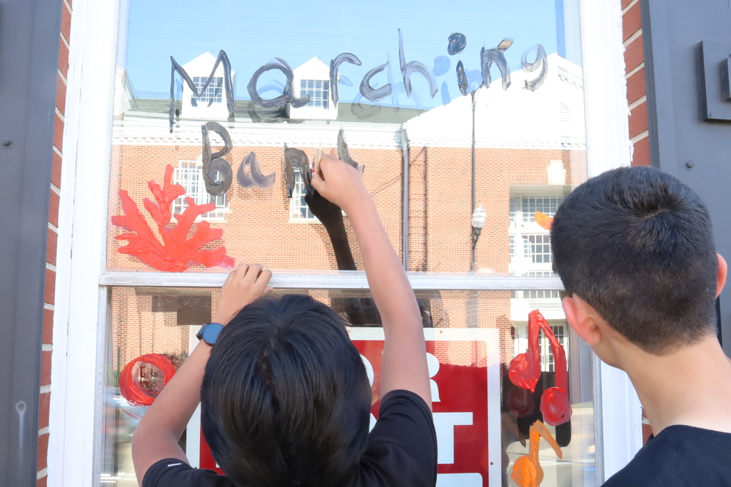 Students painting "Marching band" on window 