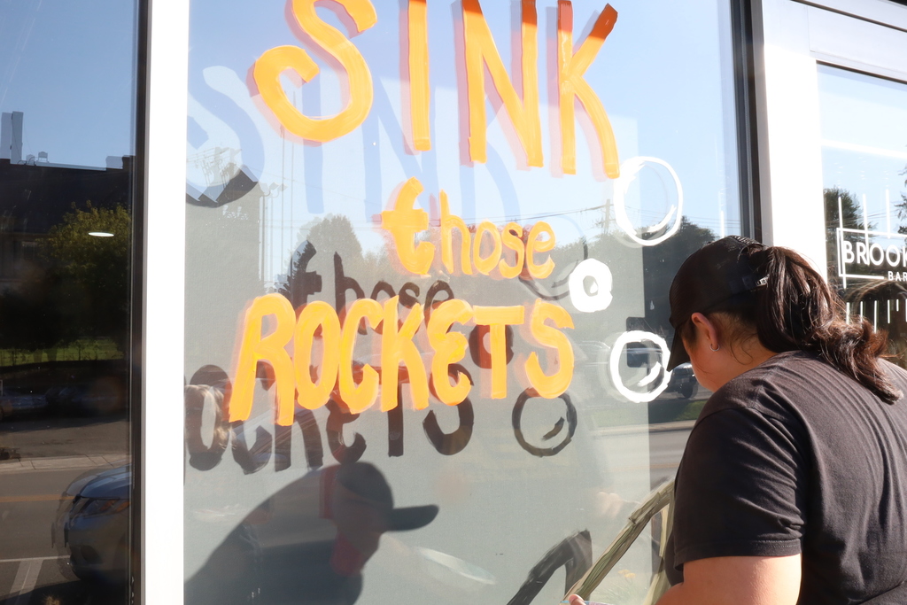 Student painting "Sink those rockets" on the window