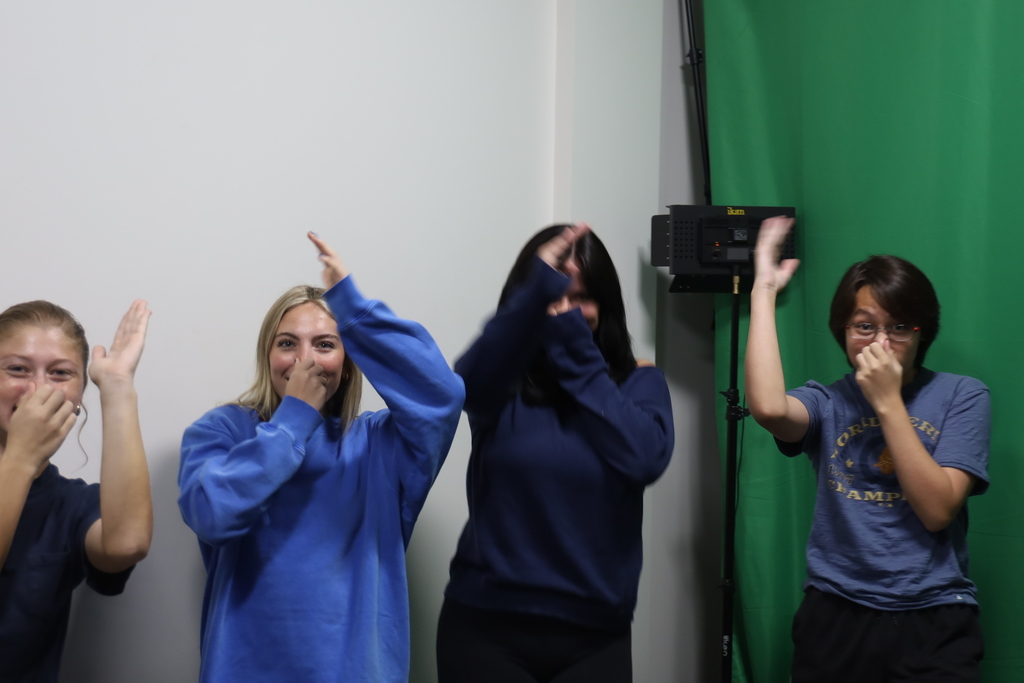 Four students plugging their noses and acting like. they're swimming, wearing blue 