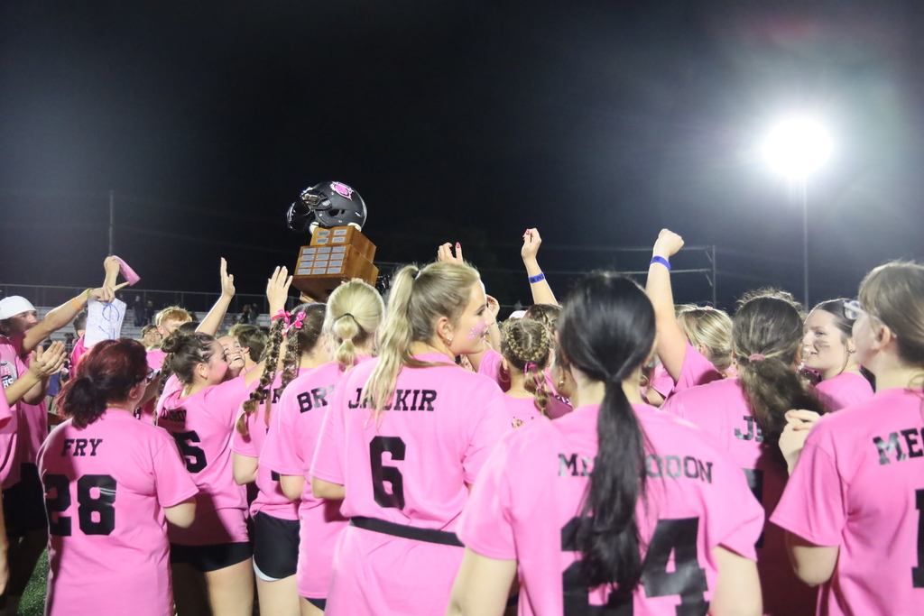 Seniors in pink Powder Puff shirts celebrating with trophy 
