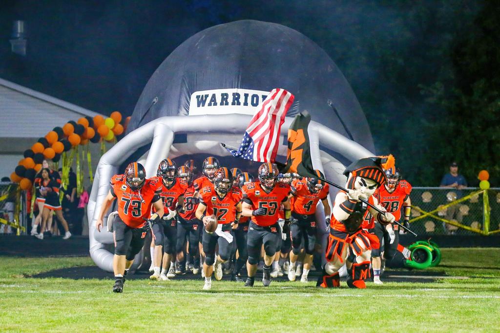 Football running under a blow up football helmet. Mascot with flags