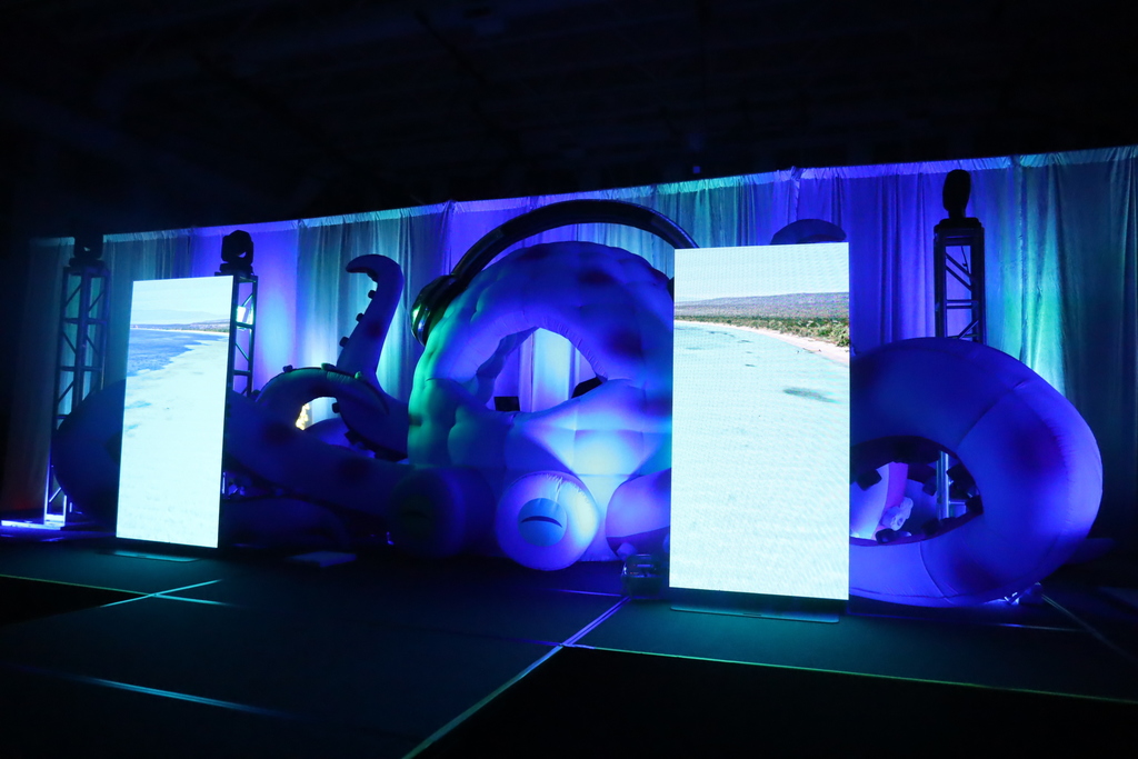 Giant octopus with headphones on with two screens with sea videos and 