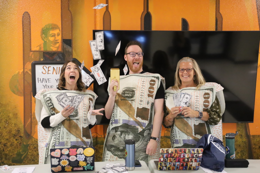 Mr. Menke shooting fake money in the are. Ms. Schak cathing it and Ms. Buchanan smiling and holding money
