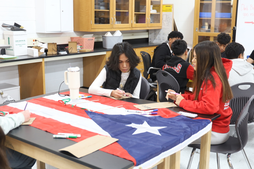 Four students drawing at a table with the a country's flag