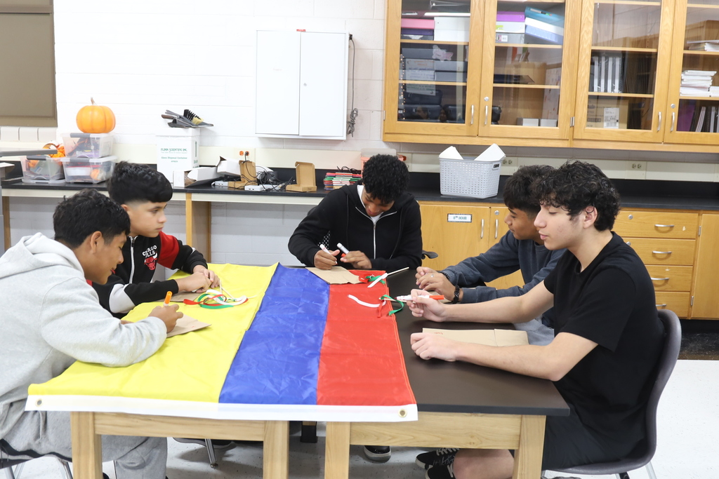 Four students drawing at a table with the a country's flag