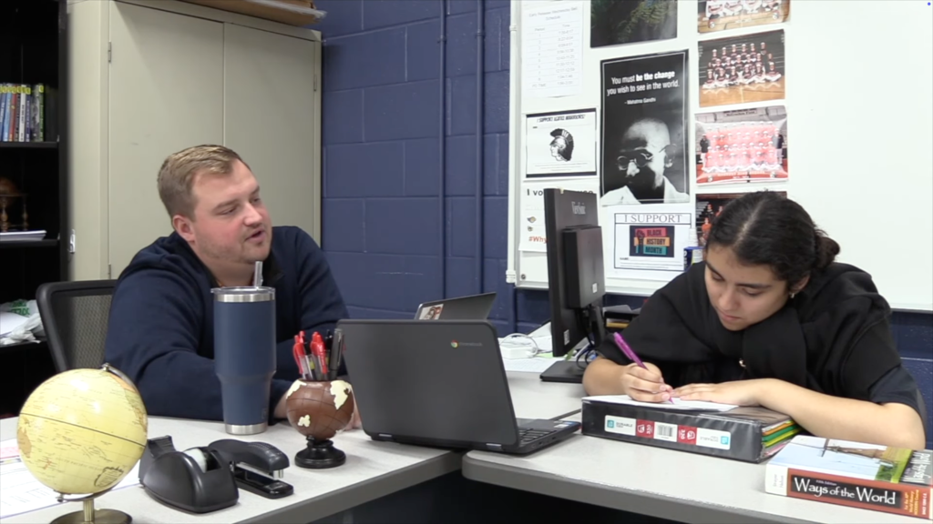 Mr. Vollmert helping a student who's writing on a paper