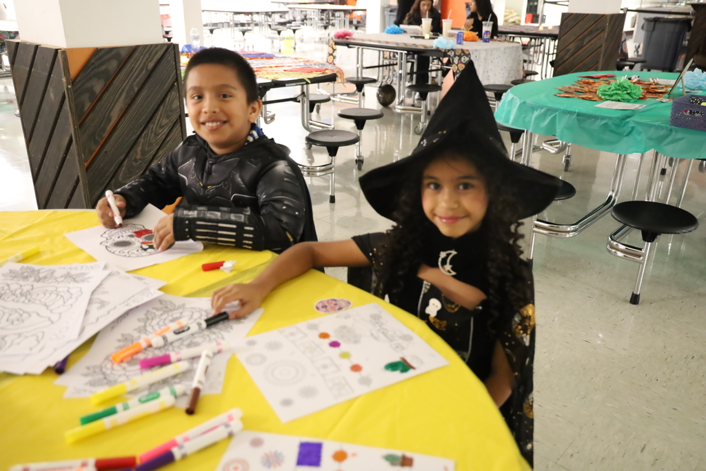 Child dressed as a witch coloring other child in a costume coloring