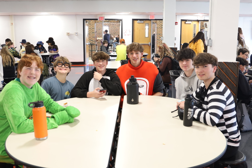 Group of students at table in costumes, one in green suit, one as ketchup one as criminal 