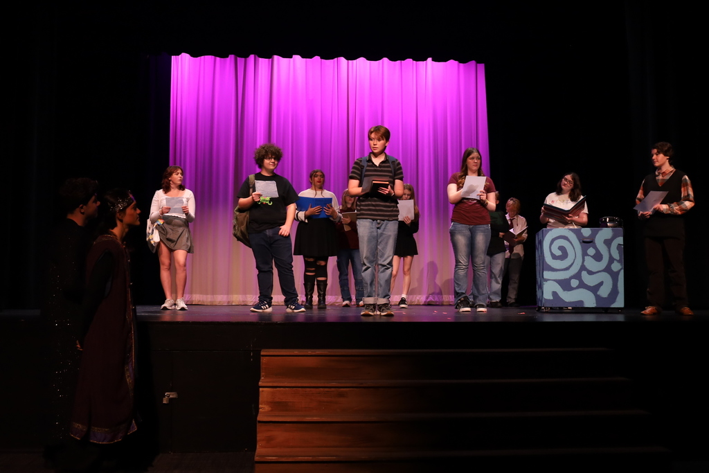 Students on stage holding papers or binders