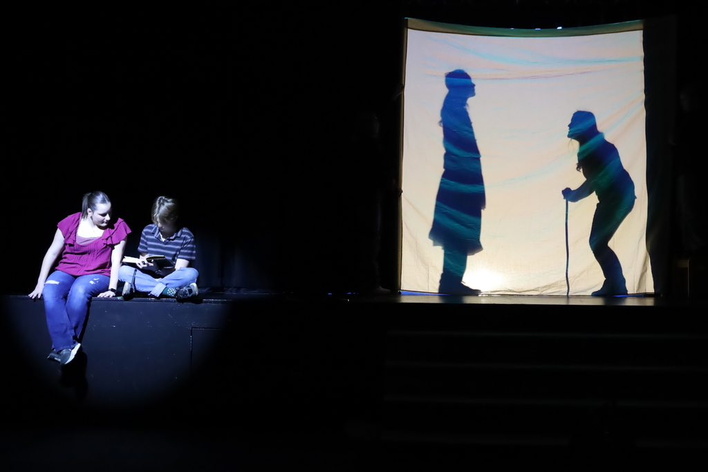 Two students reading a book with shadows of a person with a cane begging to a king