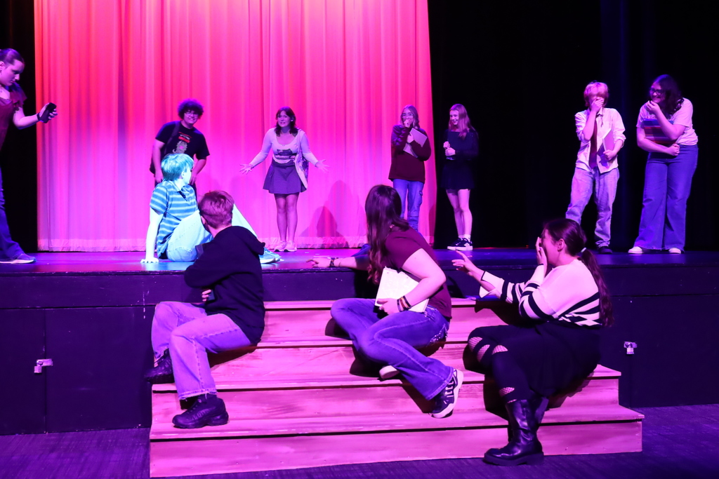 Students on stage laughing and pointing to a student who's on the ground