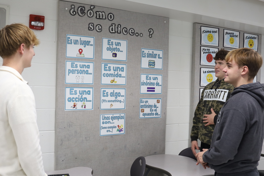 Three students talking and looking at Spanish words on a bulletin board