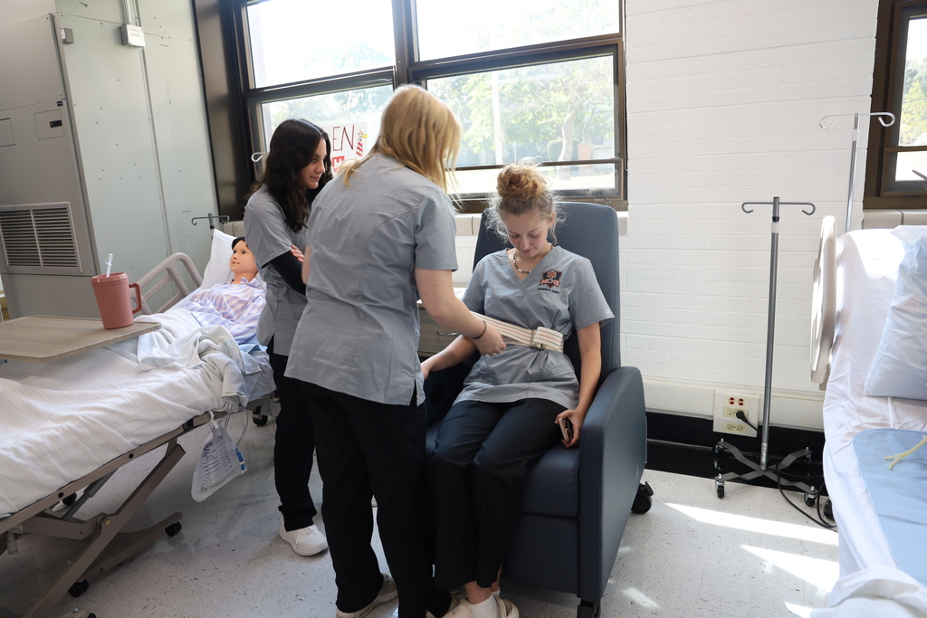 Students in CNA Class putting a lifting belt on another student 