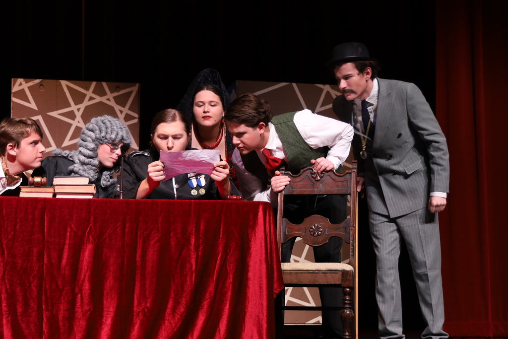 Characters all looking at a note together one dressed as a judge