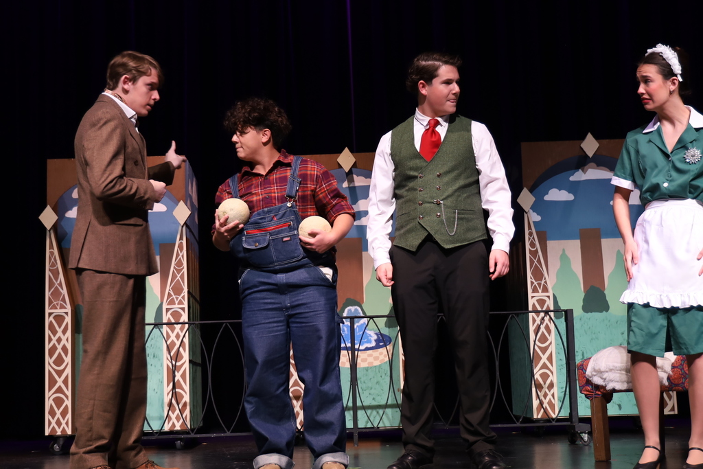 Man talking to another character with overalls holding melons the other couple looking at each other nervously