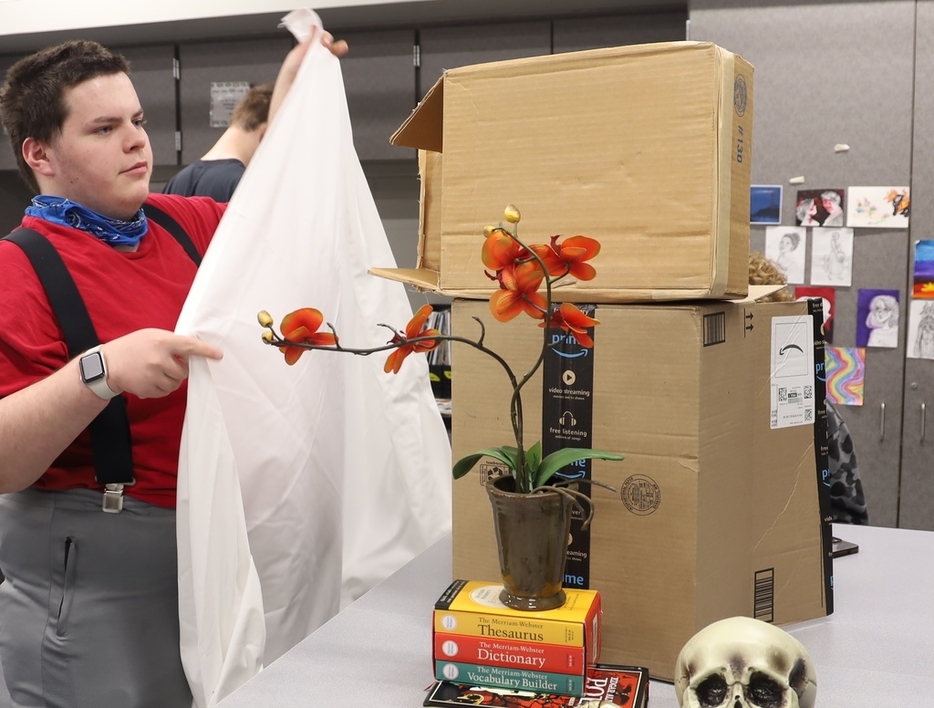 Studetn setting up still life with flower books box and skull and sheet 