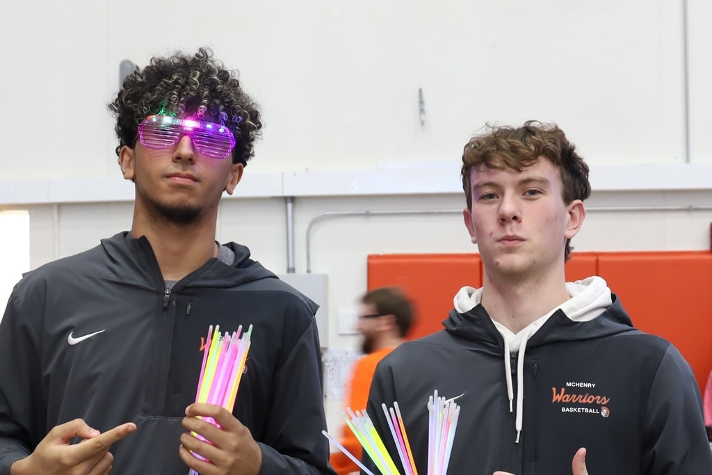 Two students holding glow sticks and one wearing colorful glasses 