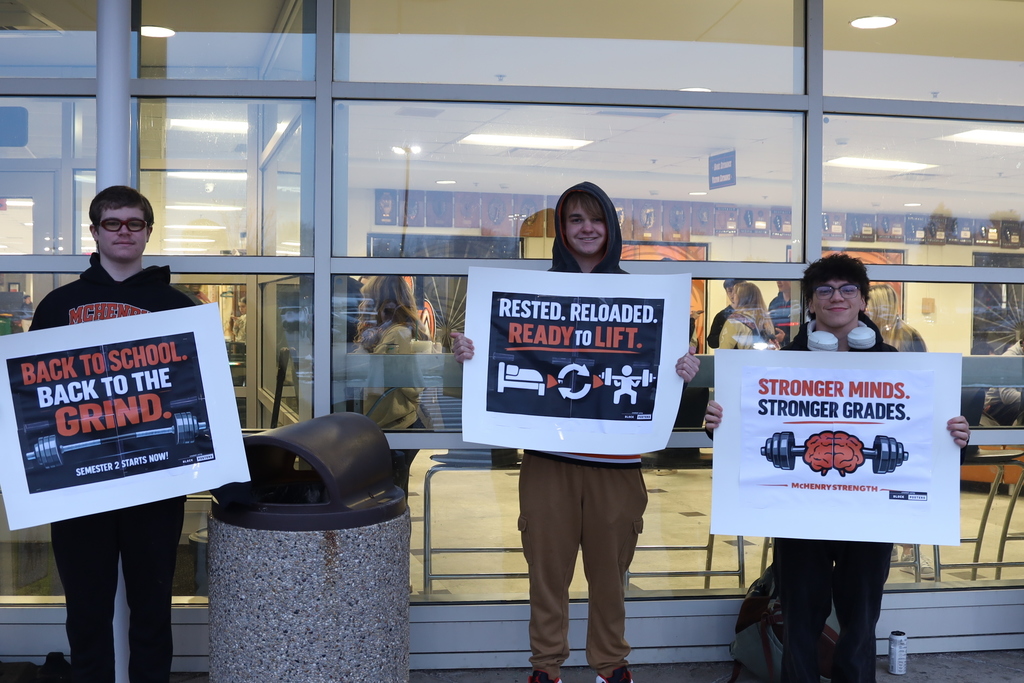 Students holding posters that say "Back to School Back to the Grind" "rested Reloaded, Ready to Lift" "Stronger Minds Stronger Grades"