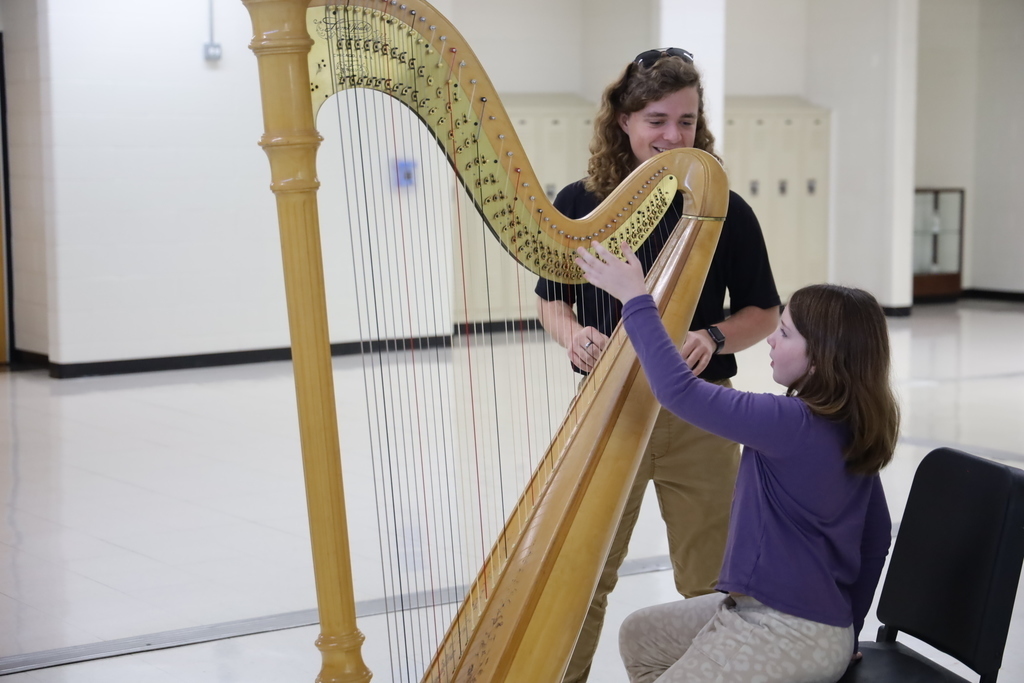 High schooler helping child play harp