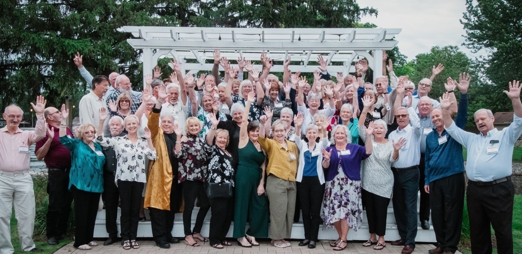People holding their hands up in the air at a group photo at a high school reunion