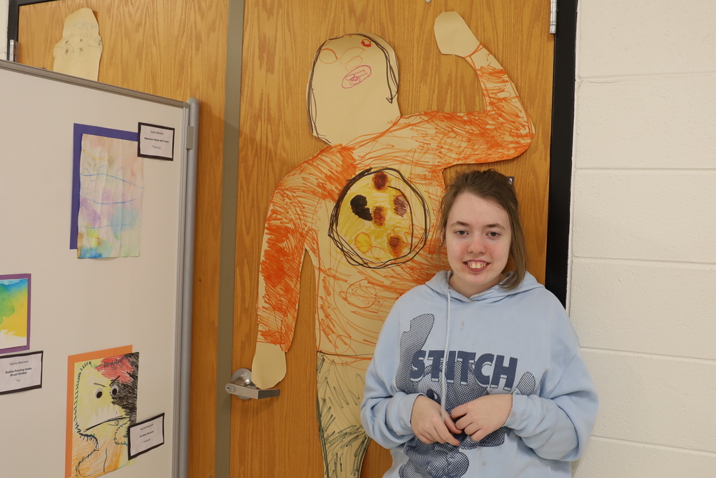  Student with their artwork large version of herself with pizza on her shirt