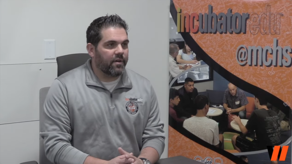 Mr. Valenziano sitting in front of Incbuator poster