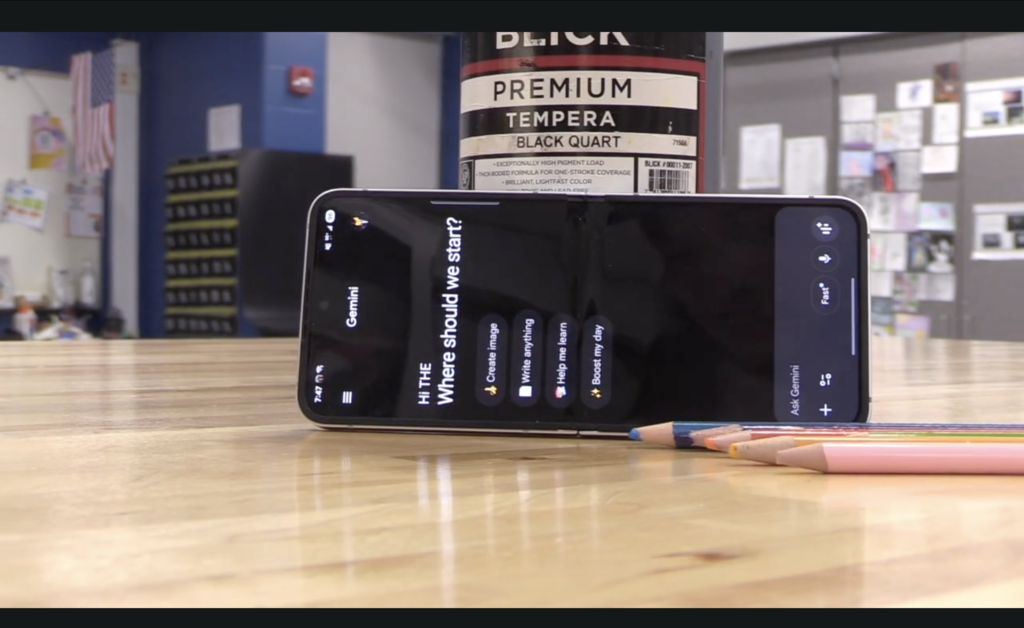 Colored pencils next to a phone with AI prompts and paint in the back 