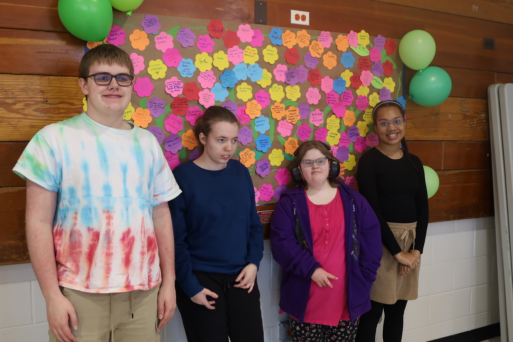 Students standing in front of inclusion wall full of flowers with what inclusion means to them