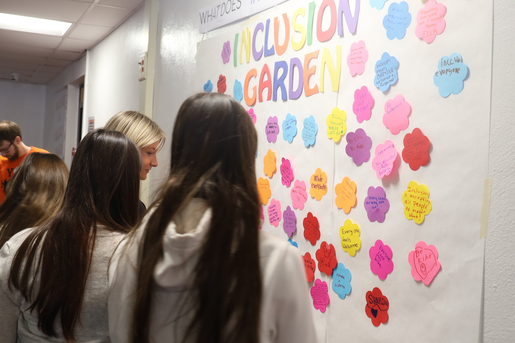Students looking at inclusion wall full of paper flowers of what inclusion means to them