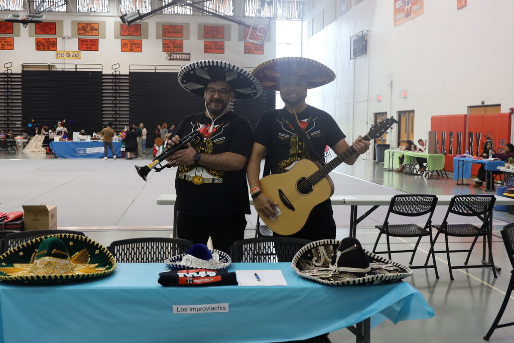 Two men with sombreros guitar and other instruments with a sign that says los improviachis 