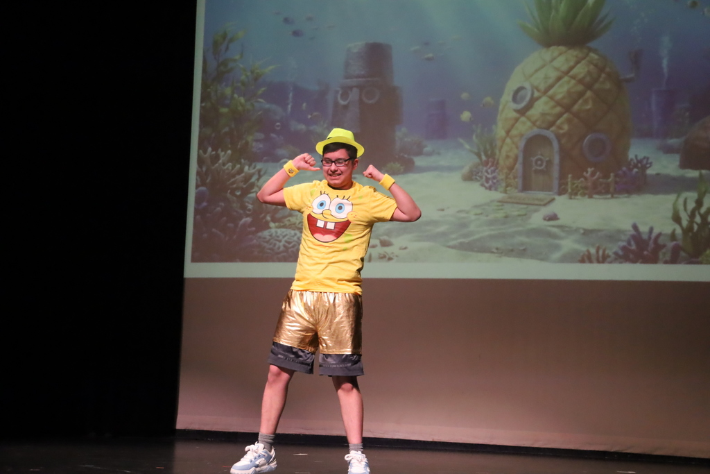 Student dressed in Spongebob shirt and yellow hat flexing muscles in front of Spongebob background