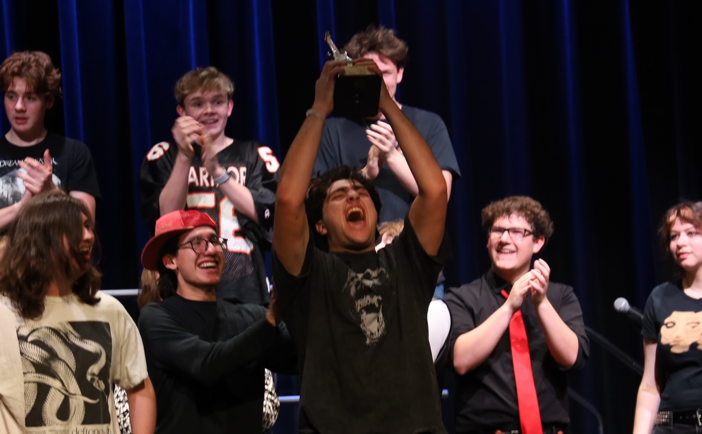 Student holding up trophy excitedly with other students around him  