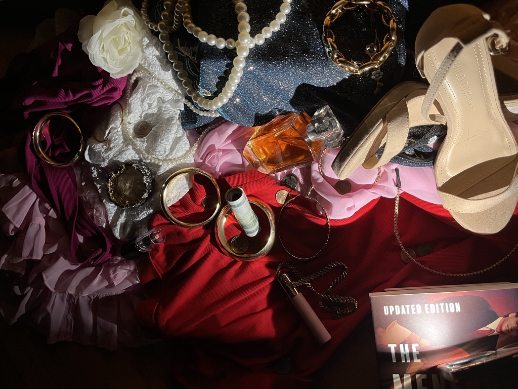 Photography of a lot of stuff laid out, book, lip gloss, heels, jewlery 