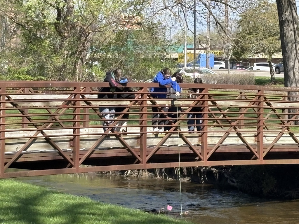Students on the bridge putting a long tool into the river