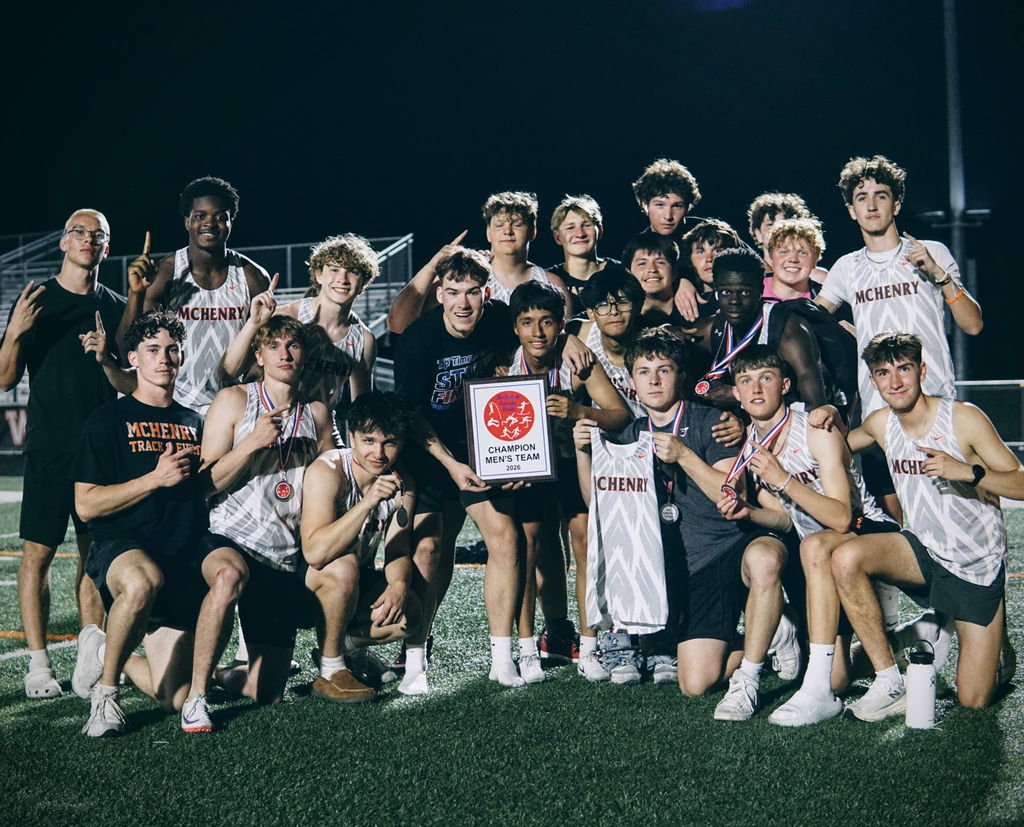 Boys track team holding up one finger for number one. Some wearing medals and two in the middle holding Champion Men's Team plaque