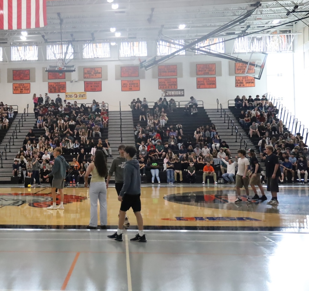 Gym full of student in bleachers with some playing dodgeball 