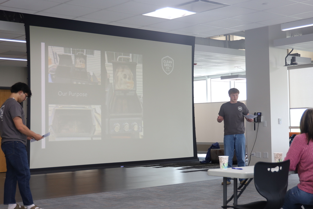 Two students presenting in front of a slide with a grill 