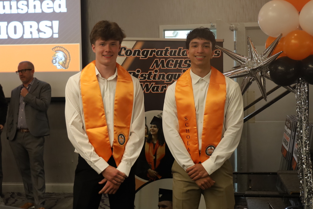 Two students with their stoles next to a congratulations sign