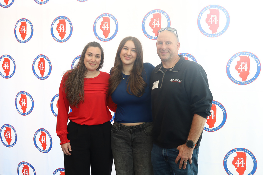 Kaitlyn with her parents in front of Regional Office of Education McHenry, IL logo backdrop